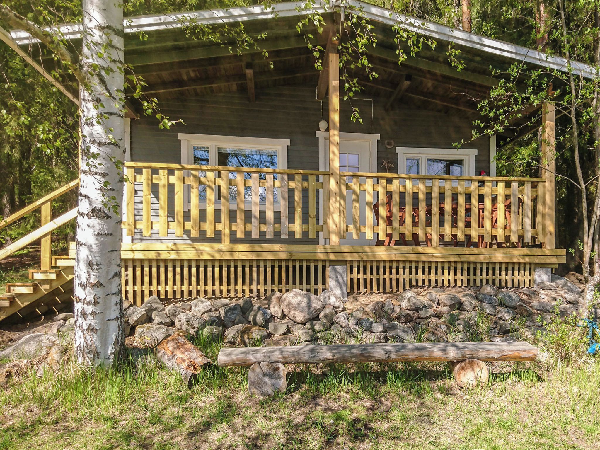 A cabin with a wooden deck, stone foundation, and a natural surrounding.