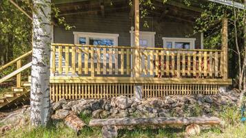 A cabin with a wooden deck, stone foundation, and a natural surrounding.