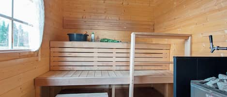 A wooden sauna room with benches, a sauna heater, and a window.
