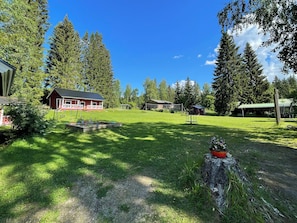 A red cabin with a fenced yard, surrounded by tall trees and a clear sky.
