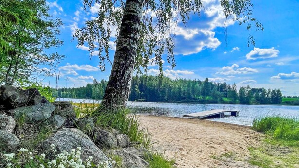 Une plage au bord d’un lac, avec un quai, entourée de rochers et de verdure.