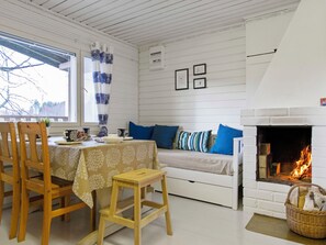 A cozy room with a white fireplace, a sofa with blue cushions, a dining table with chairs, and a window with curtains.