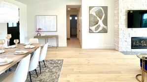 A modern living room with a fireplace, a dining area with a long table and chairs, and a hallway leading to another room.