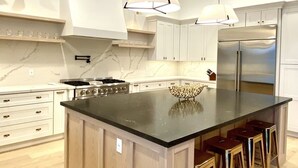 A modern kitchen with a large island, stainless steel appliances, and pendant lighting.