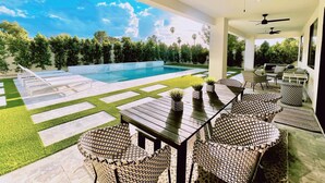 A modern outdoor patio with a pool, seating area, and ceiling fans.