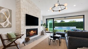 A modern living room with a fireplace, a flat-screen TV, a sofa, and a view of a pool.
