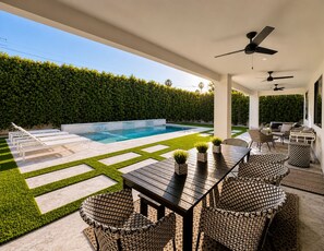 Un patio exterior cubierto con piscina, zona de estar y vistas al jardín trasero.