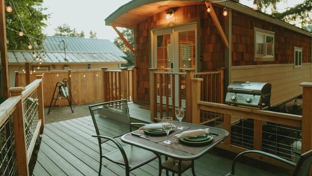 Une cabane en bois dotée d’une terrasse, d’un barbecue et d’une table dressée pour le repas.