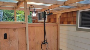 Une terrasse en bois avec un espace douche, comprenant une pomme de douche et un luminaire.