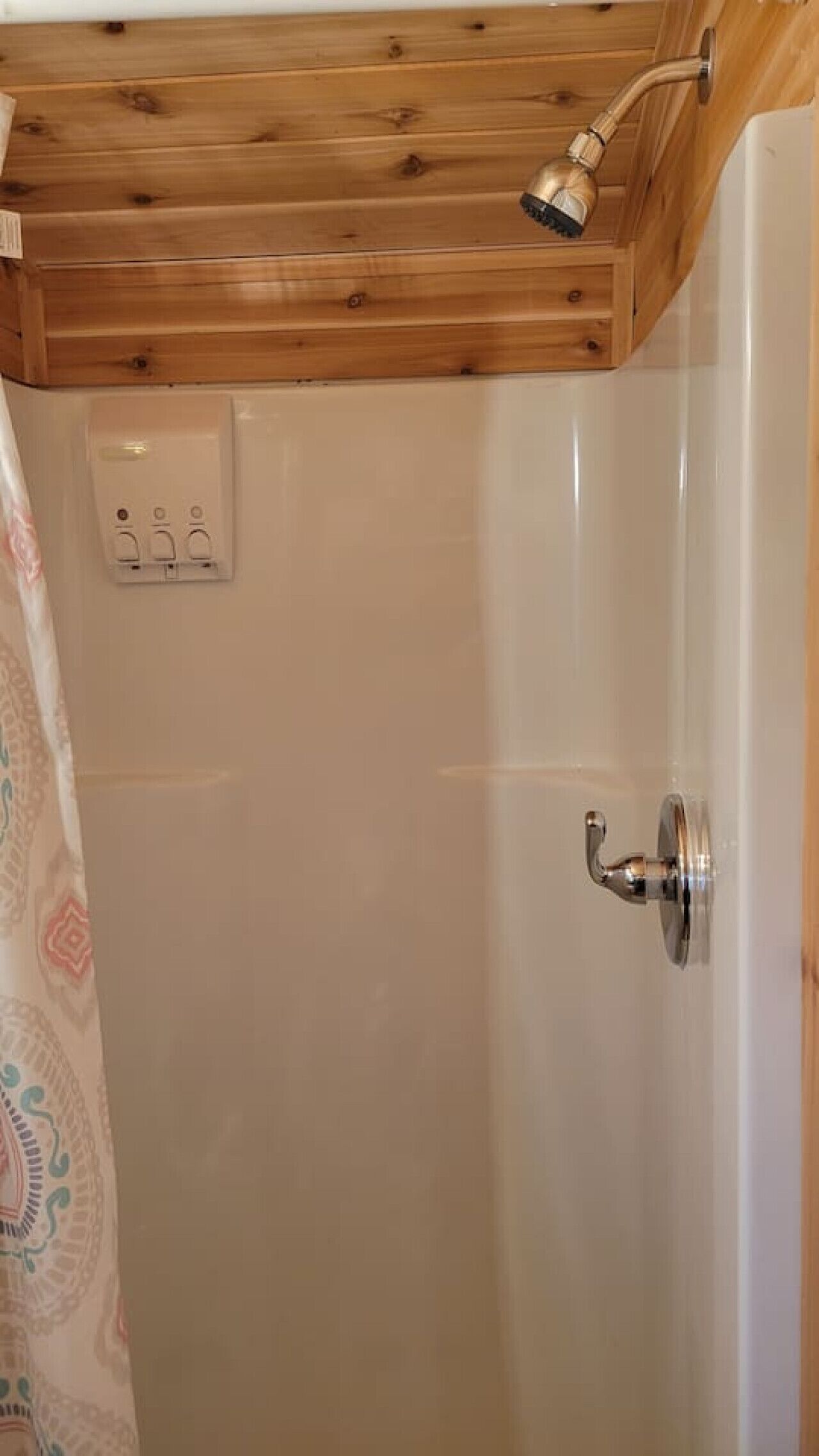Ducha con techo de madera, puerta blanca y enchufe en la pared.