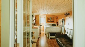Une chambre confortable avec un plafond en bois, un lit recouvert d’une courtepointe à rayures, un banc et un petit bureau avec une chaise.