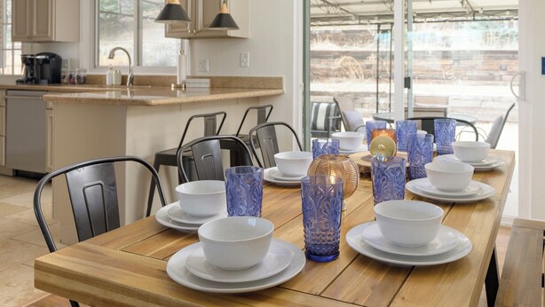 Un coin repas avec une table en bois dressée pour quatre personnes, entourée de chaises, et une cuisine en arrière-plan.