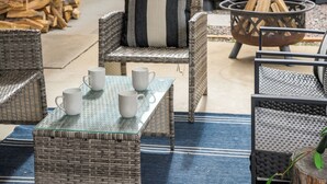 Des meubles en osier, une table avec un plateau en verre et un foyer extérieur.