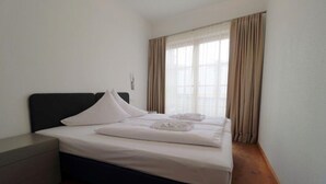 Un letto rifatto con lenzuola e cuscini bianchi, un comodino e una finestra con tende.