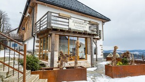 A wooden chalet with a sign reading 'Ameisberger Landhaus.' It features a staircase, large windows, and outdoor planters. - Holiday flat "Landhaus Ameisberg" with mountain view, garden and Wifi (Mitternschlag)
