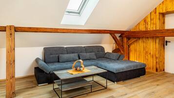 Una habitación estilo loft con techo de viga de madera, sofá seccional gris, una mesita y una pared de madera.
