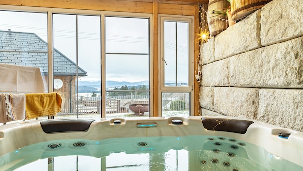 A hot tub with a view of mountains, wooden walls, and a stone wall. - Holiday flat "Landhaus Ameisberg" with mountain view, garden and Wifi (Mitternschlag)