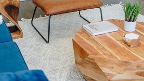 A modern living room with a brown leather chair, a blue sofa, a wooden coffee table with a book and a plant, and a patterned rug. - Comfortable and Trendy Design 1BR in Lincoln Square (Chicago)