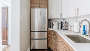 A modern kitchen with a stainless steel refrigerator, wooden cabinets, a white countertop, a coffee maker, a kettle, and a sink with a faucet. - Comfortable and Trendy Design 1BR in Lincoln Square (Chicago)