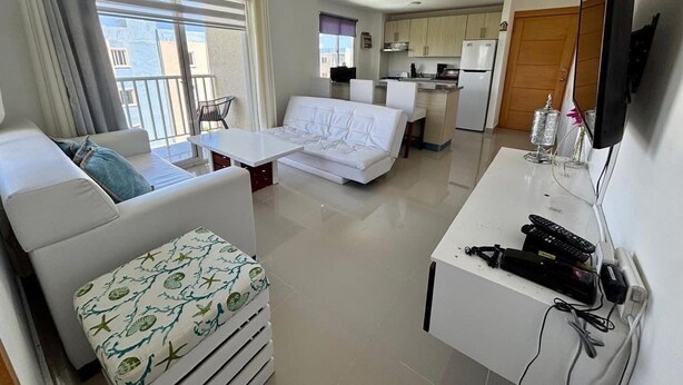Ein modernes Hotelzimmer mit Balkon, einer Küchenzeile und einer Sitzecke mit Sofa und Sesseln.