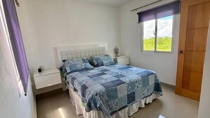 Ein Schlafzimmer mit Bett, Nachttischen, einem Fenster und einer Tür.