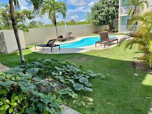 A swimming pool with lounge chairs, a grassy area, and a building in the background. - Luxury Punta Cana Retreat - Gated Community - Fast Wi-Fi (Punta Cana)