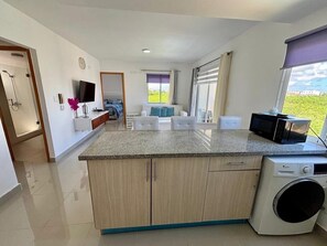 Une cuisine moderne dotée d’un plan de travail en granit, de meubles en bois, d’un lave-linge encastré et d’un coin repas offrant une vue sur l’extérieur.