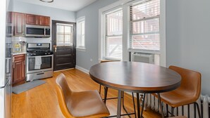 Une cuisine avec des meubles de rangement en bois, une cuisinière et un four à micro-ondes. On y trouve une table à manger avec quatre chaises.