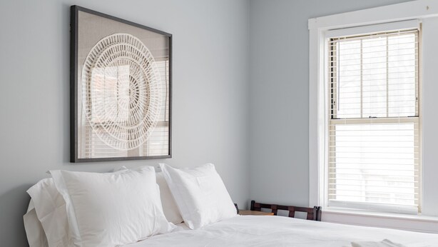 Une chambre à coucher avec un lit, des oreillers, un tableau encadré et une fenêtre avec des stores.