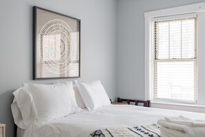 A bedroom with a bed, pillows, a framed artwork, and a window with blinds. - Charming Guest Favorite 1BR in Lincoln Square (Chicago)
