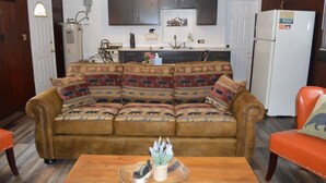 A living room with a brown sofa, a wooden coffee table, and a kitchen in the background. - Entire Bear Den (cozy cabin) close to Glacier (Essex)