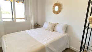 Une chambre à coucher avec un grand lit, une table de chevet, un miroir et une fenêtre avec des rideaux.