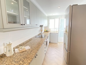 A modern kitchen with white cabinets, granite countertops, and a stainless steel refrigerator.