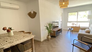 Un salon moderne avec une table à manger en bois, un canapé, un meuble pour la télévision et un luminaire suspendu.