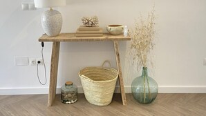 Une console en bois, sur laquelle sont posés une lampe, un bol, un petit vase contenant des plantes séchées, un panier en osier et un bocal en verre.