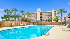 A swimming pool with lounge chairs, palm trees, and a hotel building in the background.
