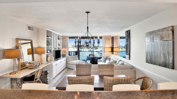 A modern living room with a large sofa, a dining table, and a chandelier. There is a television and a bookshelf in the room.