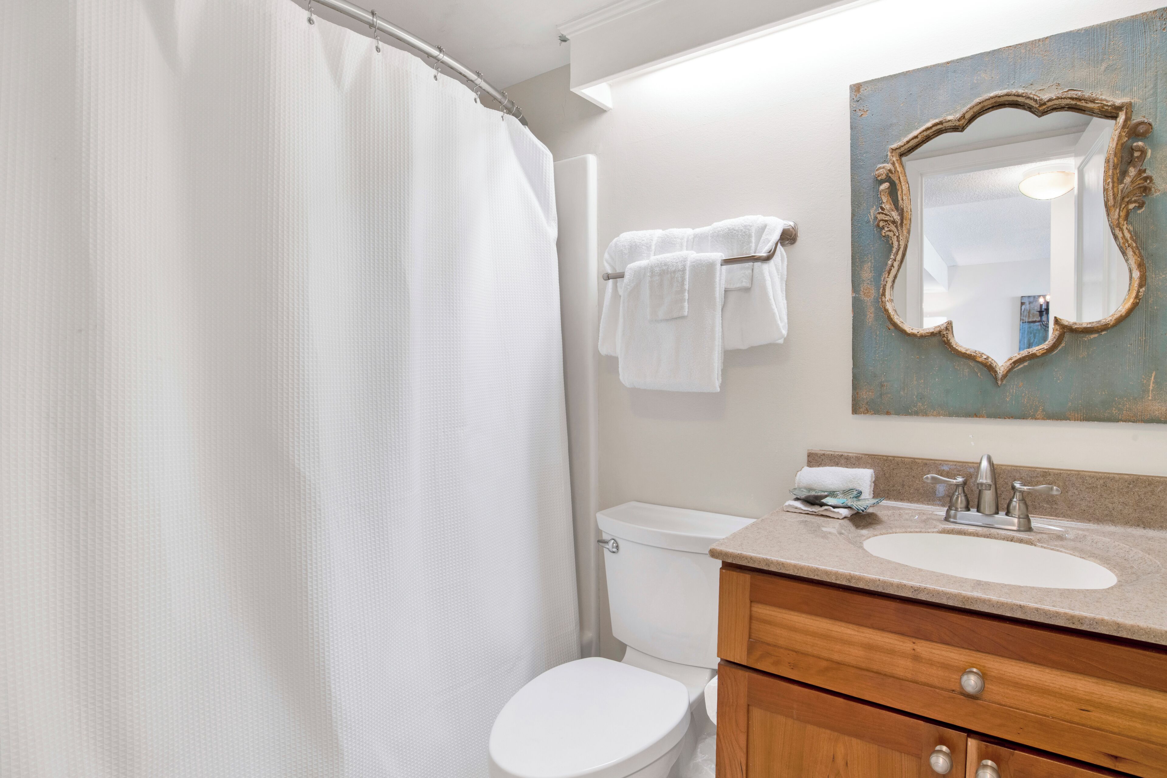 A bathroom with a shower curtain, a toilet, a sink with a mirror, and a towel rack.