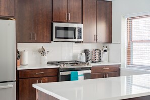Una cocina moderna con armarios de madera oscura, microondas de acero inoxidable, cocina a gas y encimeras blancas.