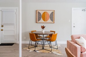 Un comedor con una mesa redonda, cuatro sillas y una obra de arte colgada en la pared.