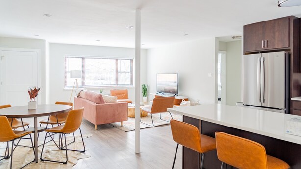A modern kitchen with a large island, a dining area with a round table and orange chairs, and a living area with a pink sofa and orange chairs. - Modern Aesthetic 2BR in Evanston Near the Beach (Evanston)