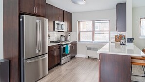 A modern kitchen with dark wood cabinets, stainless steel appliances, and a large island with bar stools. - Modern Aesthetic 2BR in Evanston Near the Beach (Evanston)