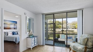 A spacious living room with a large sliding glass door leading to a balcony, a cozy seating area with a patterned armchair, and a small side table with decorative items. - Bradenton Beach/Anna Maria Island, IMG Academy, Longboat Key, Sarasota (Bradenton)