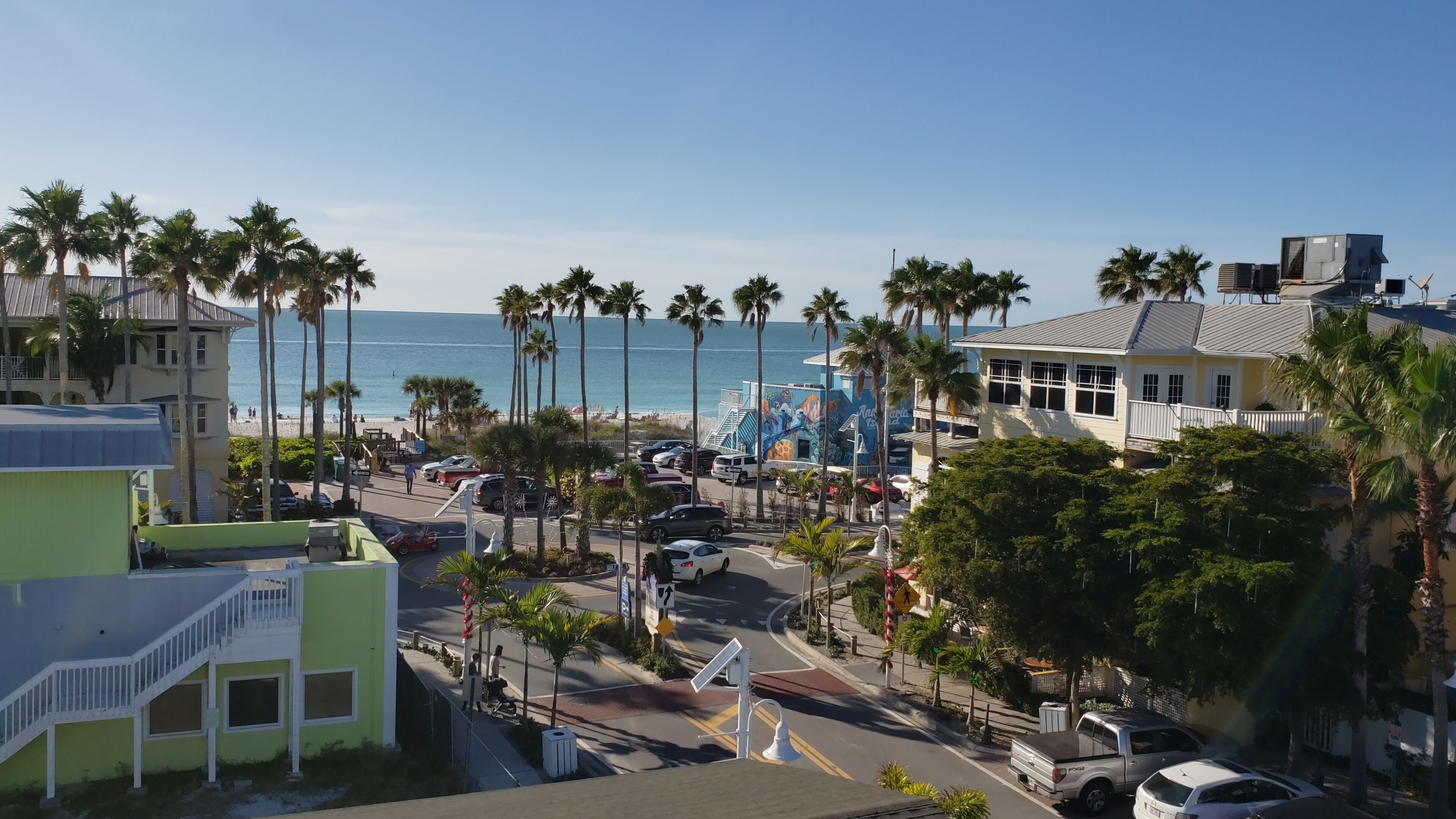A coastal street with palm trees, a beach, and a mural.