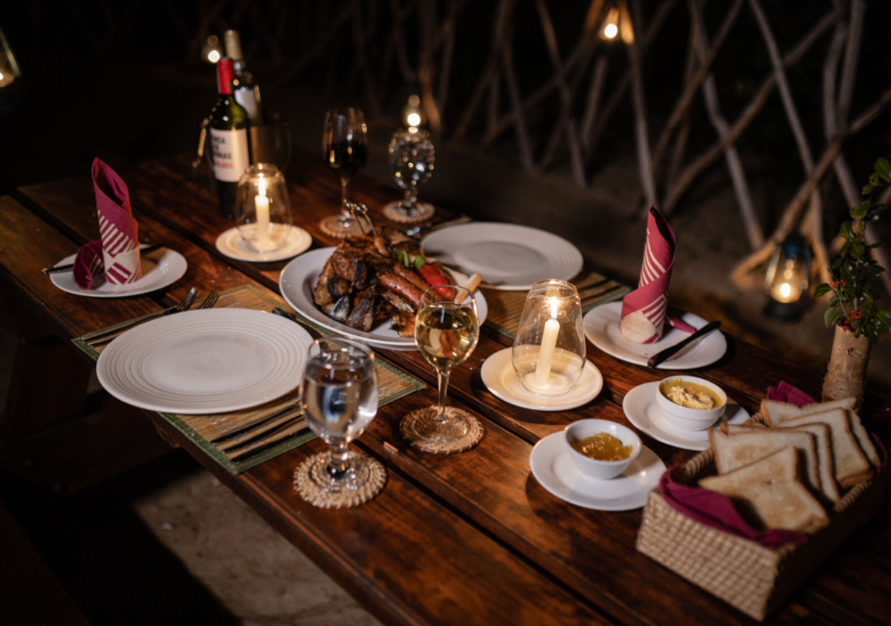 Een houten eettafel gedekt met borden, glazen, kaarsen en eten.