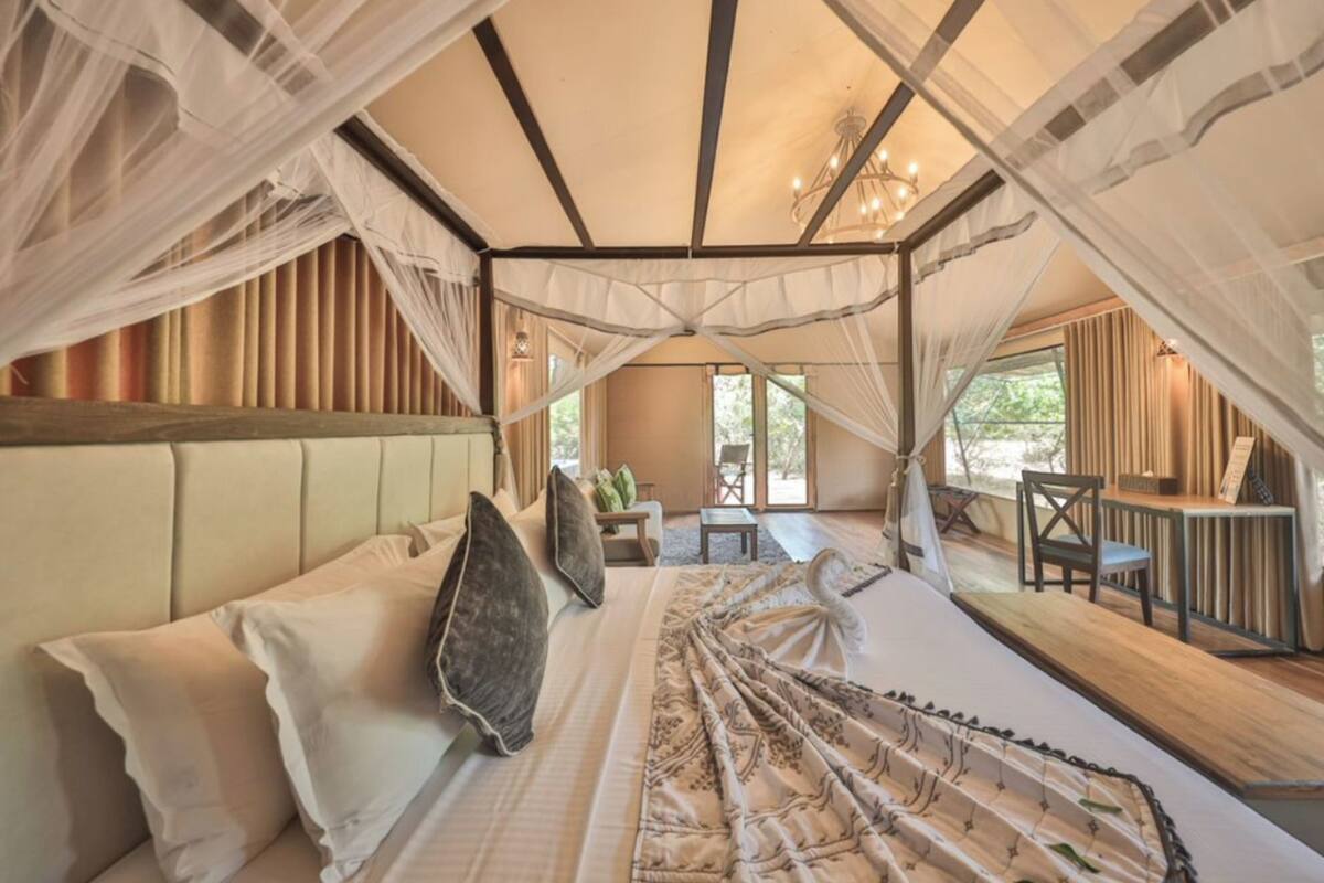 Een slaapkamer in tentstijl met een bed, kussens, een klein tafeltje en een stoel.