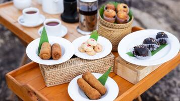 Una bandeja de madera con diversos alimentos, entre ellos croquetas, pasteles y dulces cubiertos de chocolate, sobre una mesa al aire libre.