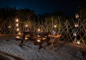 A wooden bench and picnic table set on a sandy surface, surrounded by a lattice fence with lanterns. - Tribe Yala - Luxury Camping (Thissamaharama)
