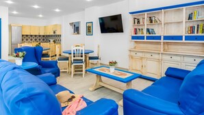 Una sala de estar con muebles azules, un comedor, una cocina y una estantería.