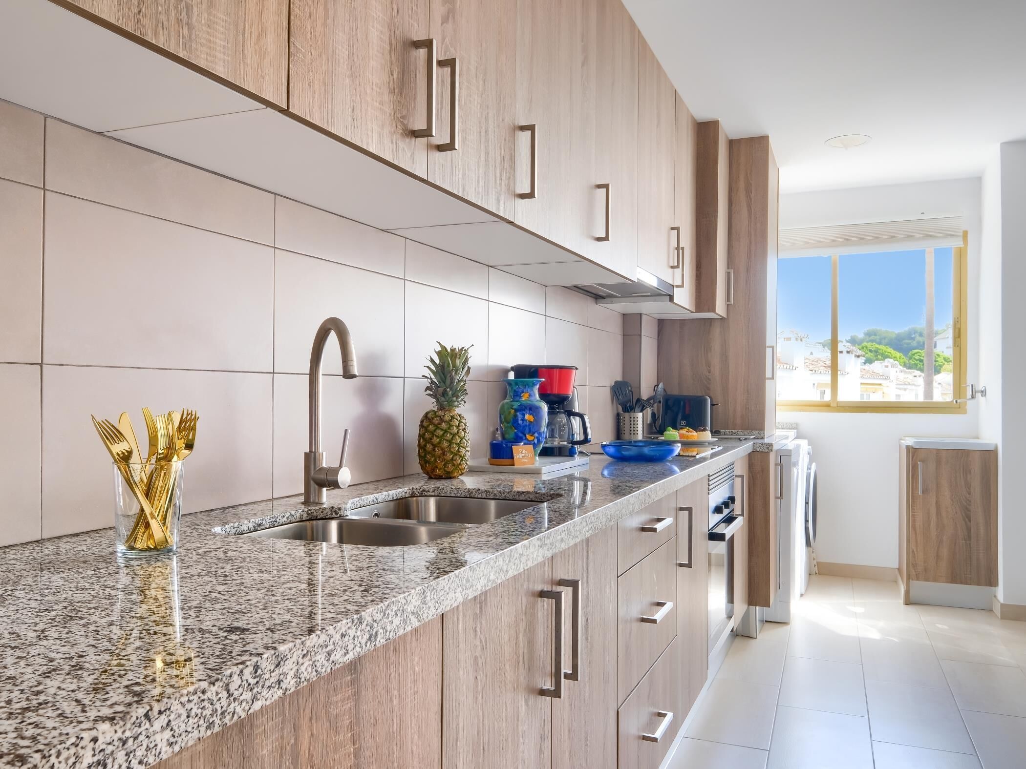 Una cocina moderna con encimeras de granito, pileta de acero inoxidable, armarios de madera y una ventana con vista a la ciudad.